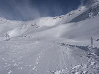 a mountain with people on skis and snowboards in the foreground, one on a cross country trail in front of the other