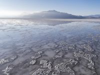 a body of water that is frozen in some land by the mountain range next to it