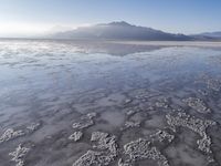 a body of water that is frozen in some land by the mountain range next to it