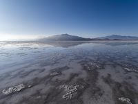 a body of water that is frozen in some land by the mountain range next to it