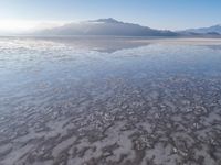 a body of water that is frozen in some land by the mountain range next to it