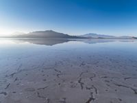 a body of water that is frozen in some land by the mountain range next to it