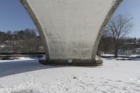 a person skis beneath a bridge and looks at the camera and snow is covering the ground