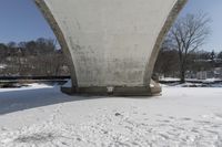 a person skis beneath a bridge and looks at the camera and snow is covering the ground