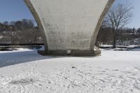 a person skis beneath a bridge and looks at the camera and snow is covering the ground