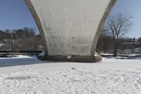 a person skis beneath a bridge and looks at the camera and snow is covering the ground