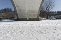 a person skis beneath a bridge and looks at the camera and snow is covering the ground