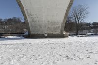 a person skis beneath a bridge and looks at the camera and snow is covering the ground