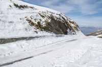 the person is standing on a mountain side road in the snow and skies over head