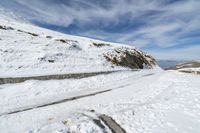 the person is standing on a mountain side road in the snow and skies over head