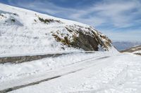 the person is standing on a mountain side road in the snow and skies over head