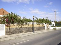 a wall on the side of a road near an empty street with plants and trees