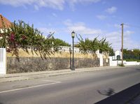 a wall on the side of a road near an empty street with plants and trees