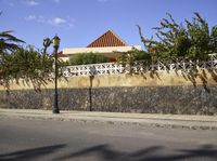 a wall on the side of a road near an empty street with plants and trees