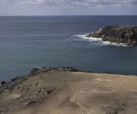 two people are sitting on the edge of a cliff above the ocean, while a group of other people swim near them