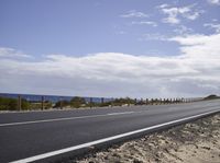 a motorcycle driving along the side of an empty road by the ocean on a sunny day