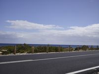 a motorcycle driving along the side of an empty road by the ocean on a sunny day