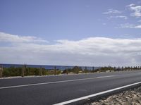 a motorcycle driving along the side of an empty road by the ocean on a sunny day