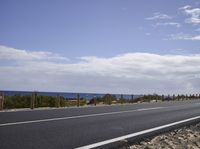 a motorcycle driving along the side of an empty road by the ocean on a sunny day