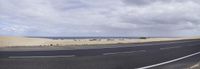 an empty street lined with black sand dunes, and a clear blue ocean to the right