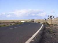 an empty road with an arrow sign pointing left and right and to the right, on the side of the road