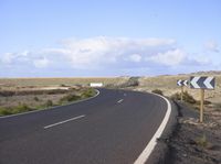 an empty road with an arrow sign pointing left and right and to the right, on the side of the road