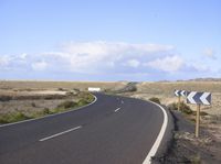an empty road with an arrow sign pointing left and right and to the right, on the side of the road