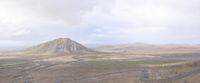 a long winding road running through a desert area with a mountain behind it on a cloudy day