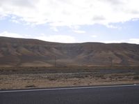 a road next to a large hill that is covered in dirt with hills in the background