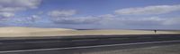 a road with a car going through the sand dunes along it and one side facing the distance