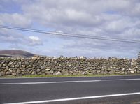 a tall stone wall by the road in the countrysides with electrical wires overhead it