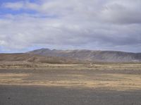 an empty deserted area has two elephants walking across it and there are mountains in the background