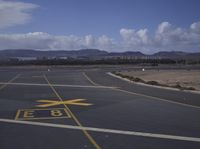 a yellow traffic signal next to an airport runway with mountains in the background and blue sky