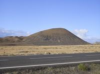 a small hill sitting in the middle of a large plain with a car passing by it