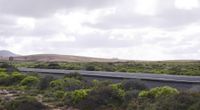 the landscape features trees, bushes and hills, along a highway in new zealand at a speed limit