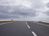 a road stretches into the distance against a cloudy sky near an empty beach area area