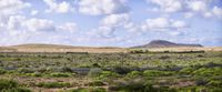 a highway runs through a vast desert plain with mountains in the distance and clouds overhead