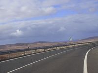 the road has two sides of it as it passes over mountains in the distance, and an empty bench beneath it