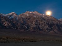 the full moon is above a mountain range in the distance with a horse grazing beneath