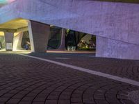 a paved path at night leading to an illuminated building with colorful lights and pillars in a lit city