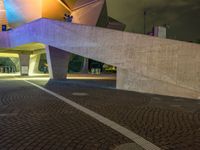 a paved path at night leading to an illuminated building with colorful lights and pillars in a lit city