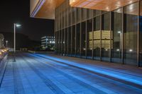 blue illuminated city street with modern architecture in the background at night, with light on the walkway and windows