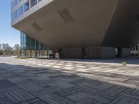 the concrete and glass walkway runs in front of a building with multiple floors and a stone floor