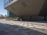 the concrete and glass walkway runs in front of a building with multiple floors and a stone floor