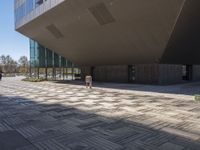 the concrete and glass walkway runs in front of a building with multiple floors and a stone floor