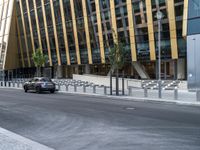 a car driving by a city building with metal barrier posts on the side of it