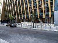 a car driving by a city building with metal barrier posts on the side of it