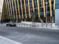 a car driving by a city building with metal barrier posts on the side of it