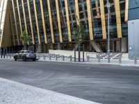 a car driving by a city building with metal barrier posts on the side of it