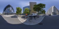 a 360 - lens view of bikes parked at a plaza outside a modern building and some buildings